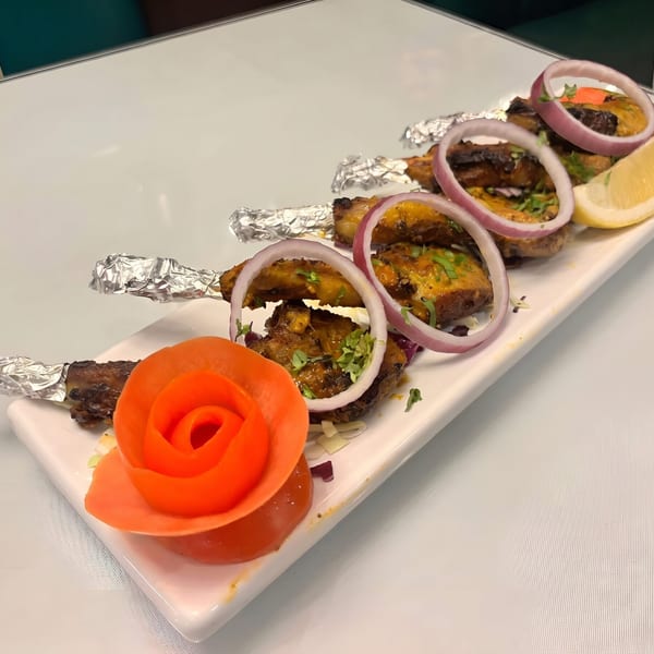 Five chicken lollipops with foil-wrapped bones, garnished with red onion rings, cilantro, and a lemon wedge.