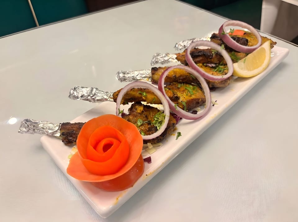 Five chicken lollipops with foil-wrapped bones, garnished with red onion rings, cilantro, and a lemon wedge.